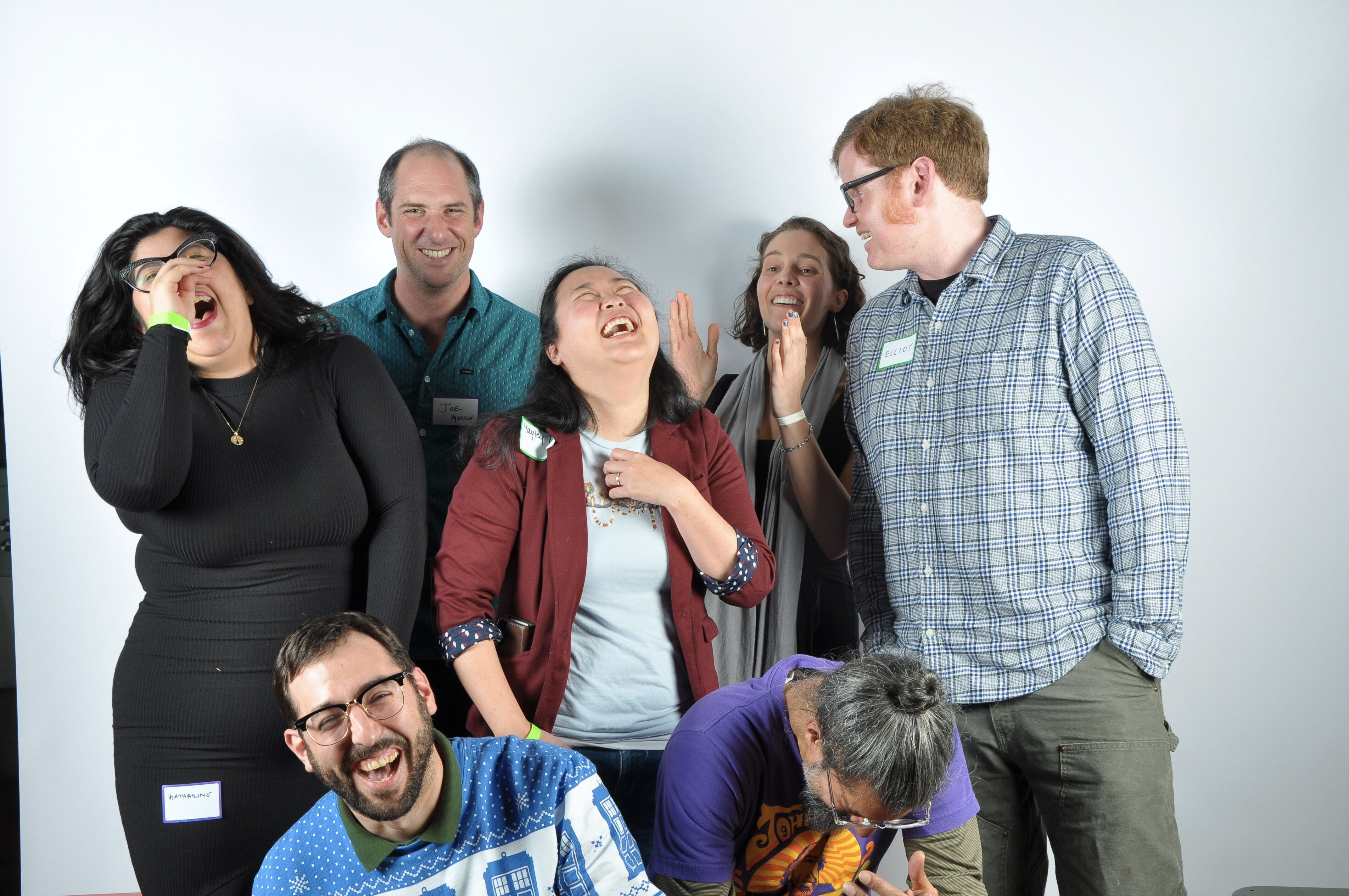 'I do not remember what Elliot said to provoke this reaction, but it’s how I will remember him.' Elliot is turned to the side, speaking to the other six people, who are laughing. He has red hair, and is wearing glasses and a flannel shirt.